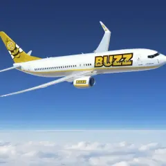 Samolot Buzz, należący do Ryanair, leci nad chmurami. Słońce odbija się od białego kadłuba, a na ogonie widnieje uśmiechnięta pszczoła. Idealny na wakacje z bagażem!