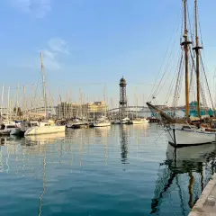Port w Barcelonie z żaglówkami i wieżą widokową w tle.