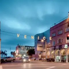 Nocny widok na Venice Beach z neonowym napisem "VENICE" i budynkami hosteli.