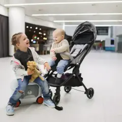 Dwie dziewczynki, jedna siedzi na walizce, druga w wózku, gotowe na podróż z Ryanair. Wózek dla 3 latka idealny na lotnisko.