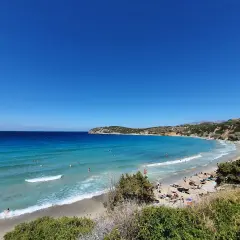 Słoneczny dzień na plaży Voulisma. Turkusowa woda, piaszczysty brzeg i zielone wzgórza tworzą idylliczny krajobraz.