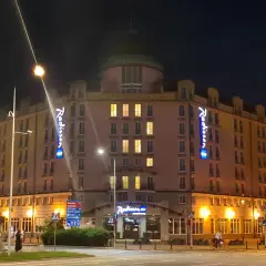 Nocą oświetlony Radisson Blu Sobieski Hotel Warsaw z neonami "Radisson" i napisem "HOTEL SOBIESKI".
