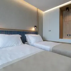 Przytulny pokój z dwoma łóżkami w hotelu Sunce Neum. Jasne ściany, nowoczesne oświetlenie i drewniane akcenty tworzą relaksującą atmosferę.