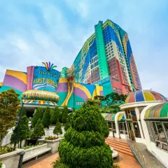 Kolorowy budynek z napisem "HOTEL FIRST WORLD" – największy hotel na świecie, otoczony zielenią i tęczowymi kopułami.