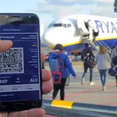 Ręka trzyma smartfon z kartą pokładową Ryanair. W tle samolot i pasażerowie.