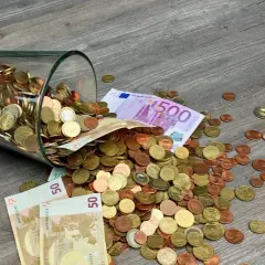 Słoik z monetami i banknotami, w tym 500 euro, rozsypany na drewnianej podłodze. To waluta Francji i innych krajów strefy euro.