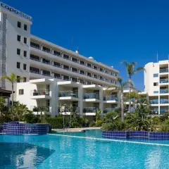 Basen hotelowy Capo Bay w Protaras z palmami i białymi budynkami hotelowymi pod błękitnym niebem.