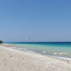 Plaża w zatoce Ialyssos, z turkusową wodą i kilkoma kitesurferami na horyzoncie.