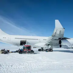 Biały airbus a340-300 na śniegu, z obsługą naziemną i ratrakiem.
