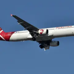 Samolot linii lotniczych Electra Airways z czerwonym ogonem i białym kadłubem leci na tle błękitnego nieba.