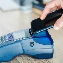 Zbliżenie na dłoń zbliżającą smartfon do terminala płatniczego. Szybka płatność za zakupy, nawet gdy używasz gruzińskiej waluty.