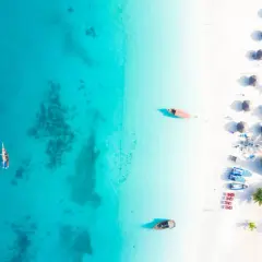 Rajska plaża na Zanzibarze, gdzie turkusowa woda i biały piasek tworzą idealne tło dla tradycyjnych łodzi. Można tu poczuć atmosferę wakacji, marząc o przygodach i wymieniając się wrażeniami, jakby to była lokalna waluta.