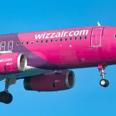 Różowy samolot Wizzair z fioletowymi elementami na tle błękitnego nieba.