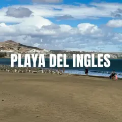 Piękna plaża Playa del Inglés z rzędami leżaków i kilkoma spacerującymi ludźmi. W tle widać hotele i góry.