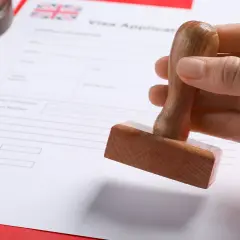 Dłoń trzyma pieczątkę nad formularzem wniosku o wizę do UK.
