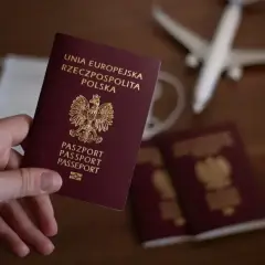 Dłoń trzyma polski paszport. Obok leżą kolejne dokumenty, maseczka i model samolotu. Zastanawiasz się, ile się czeka na paszport?