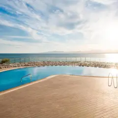 Basen przy hotelu Best Negresco z widokiem na morze i leżakami. Słońce odbija się w wodzie.