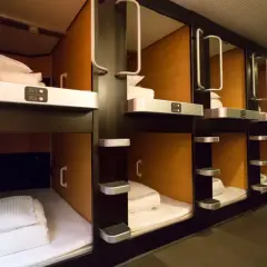 Rzędy przytulnych kapsuł w hotelu kapsułowym, każda z czystą pościelą i numerem.