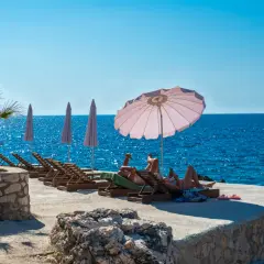 Relaks na plaży w Czarnogórze. Czy czarnogóra jest bezpieczna? Turyści odpoczywają na leżakach przy turkusowym morzu.