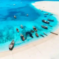 Turkusowa woda i biała plaża Malediwów, idealne miejsce na tanie loty na Malediwy. Wiele łodzi czeka na podróżnych.