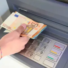 Dłoń trzyma banknoty 50 euro, walutę Hiszpanii, przy bankomacie.