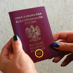 Dłonie trzymają polski paszport biometryczny z symbolem aparatu.