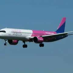 Samolot Wizz Air z różowym i niebieskim ogonem leci na tle błękitnego nieba.