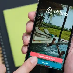 Dłoń wybiera opcję "Log In" na ekranie telefonu z aplikacją Airbnb. Czy Airbnb jest bezpieczne? To pytanie zadaje sobie wielu podróżnych.