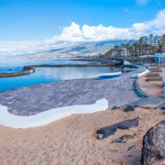 Słoneczna playa de las americas z basenem, piaskiem i kolorowymi budynkami w tle.