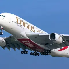 Ogromny Airbus A380 800 linii Emirates z wysuniętym podwoziem wznosi się na tle błękitnego nieba.