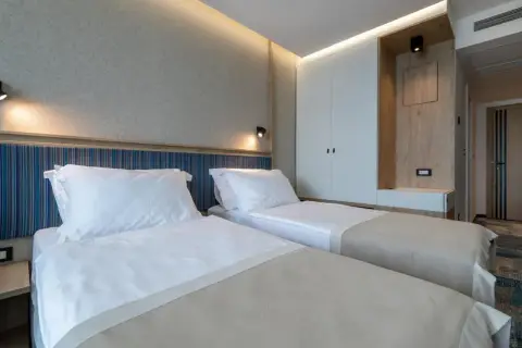 Przytulny pokój z dwoma łóżkami w hotelu Sunce Neum. Jasne ściany, nowoczesne oświetlenie i drewniane akcenty tworzą relaksującą atmosferę.
