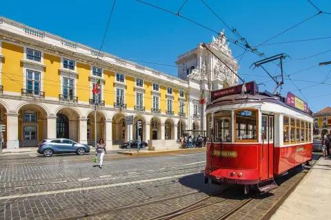 Czerwony tramwaj w Lizbonie, obok żółtego budynku i łuku triumfalnego. Czy do Portugalii potrzebny jest paszport? Tak, jeśli nie jesteś obywatelem UE.