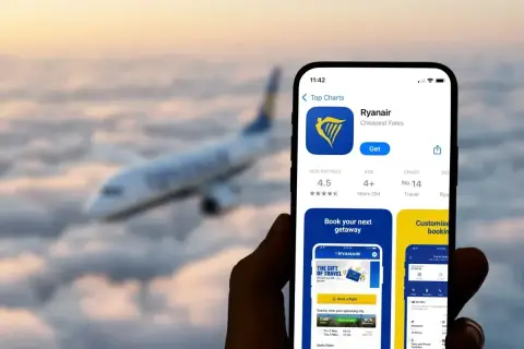 Aplikacja Ryanair na telefonie, z samolotem w tle. Czy Ryanair jest bezpieczny? Aplikacja ma ocenę 4.5 gwiazdki.