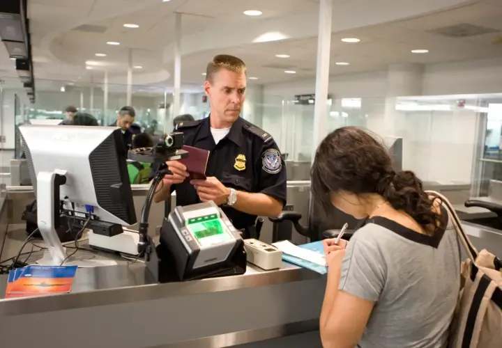Funkcjonariusz sprawdza paszport kobiety przy stanowisku check-in na lotnisku.