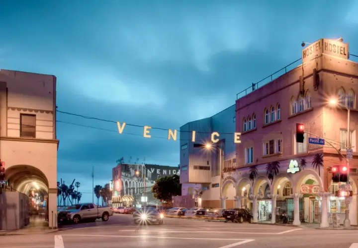 Nocny widok na Venice Beach z neonowym napisem "VENICE" i budynkami hosteli.