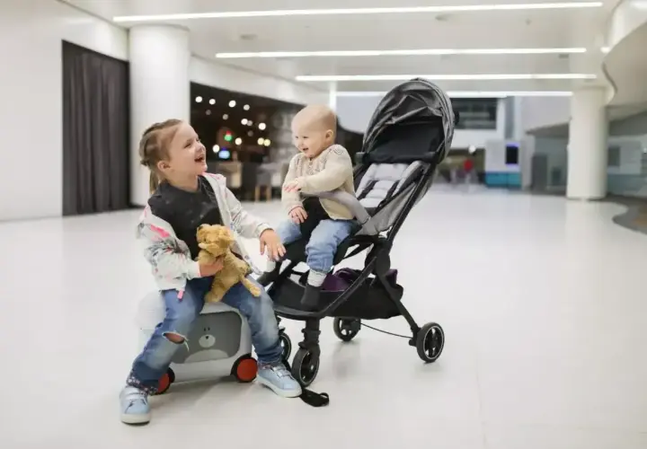 Dwie dziewczynki, jedna siedzi na walizce, druga w wózku, gotowe na podróż z Ryanair. Wózek dla 3 latka idealny na lotnisko.