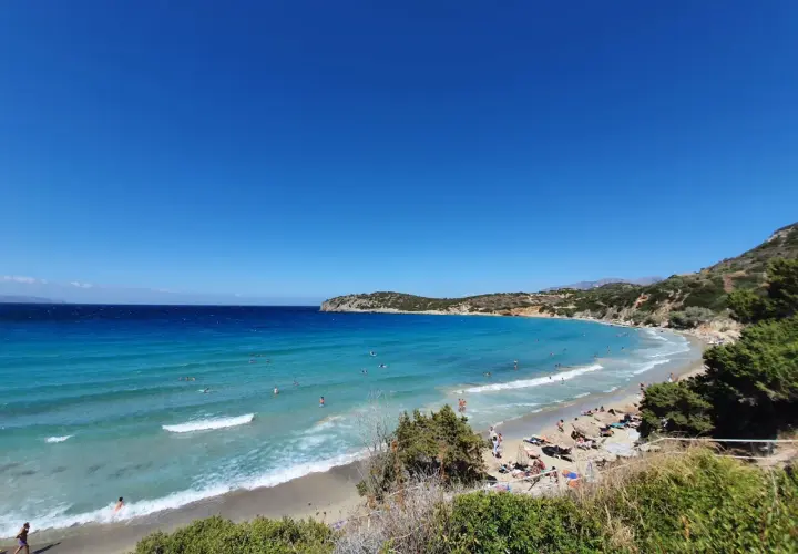 Słoneczny dzień na plaży Voulisma. Turkusowa woda, piaszczysty brzeg i zielone wzgórza tworzą idylliczny krajobraz.