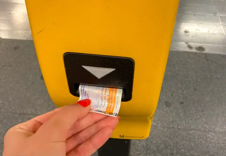 Dłoń z czerwoną hybrydą wkłada bilet do żółtego automatu w praskim metrze. Bilety na metro w Pradze są łatwe do kupienia.