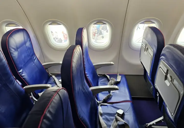 Puste siedzenia w samolocie Wizzair, przez okna widać ludzi na płycie lotniska. Automatyczna odprawa Wizzair przebiegła sprawnie.