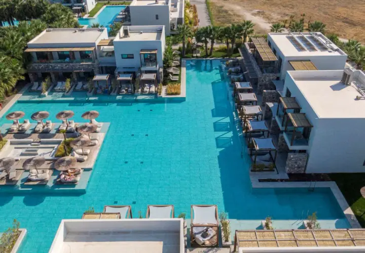 Luksusowy resort z basenami i leżakami przy plaży Caravia Beach Kos. Palmy i nowoczesna architektura tworzą idealne miejsce na relaks.