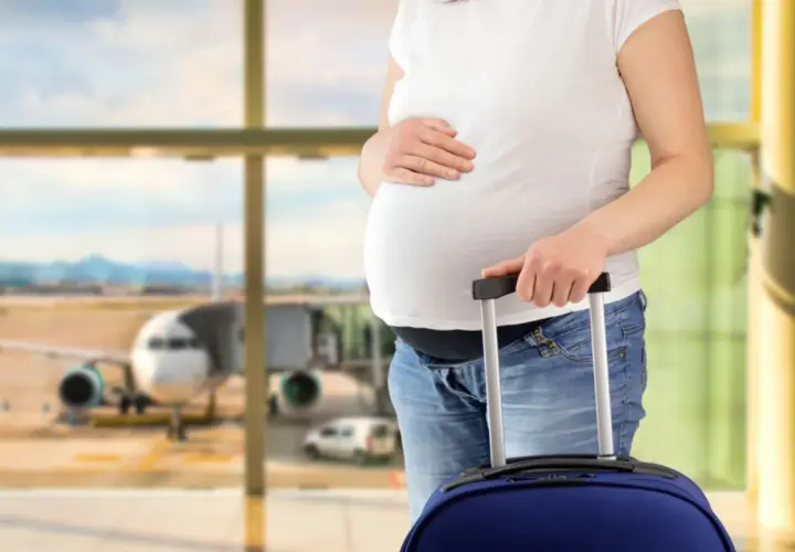 Ciężarna kobieta z walizką na lotnisku, gotowa do podróży. Wygląda na to, że jest fit to fly.
