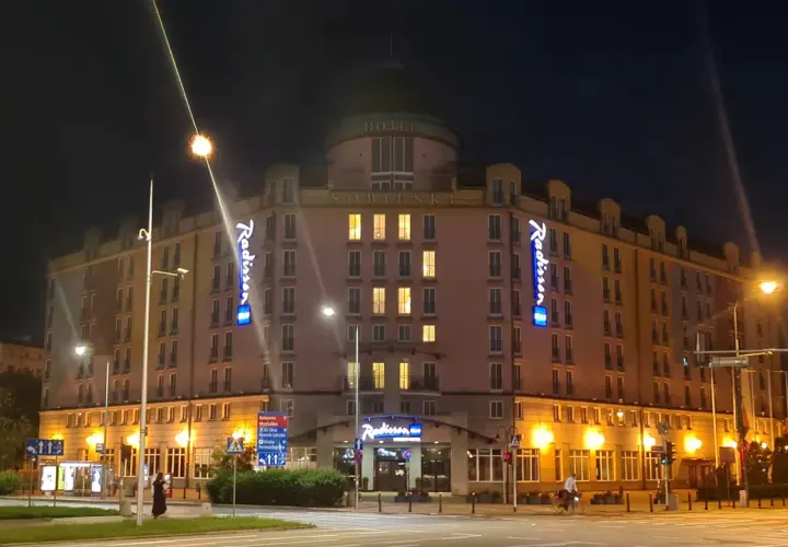 Nocą oświetlony Radisson Blu Sobieski Hotel Warsaw z neonami "Radisson" i napisem "HOTEL SOBIESKI".