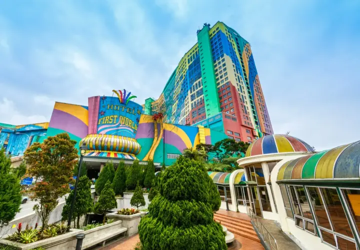 Kolorowy budynek z napisem "HOTEL FIRST WORLD" – największy hotel na świecie, otoczony zielenią i tęczowymi kopułami.
