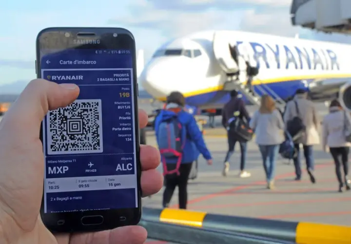 Ręka trzyma smartfon z kartą pokładową Ryanair. W tle samolot i pasażerowie.