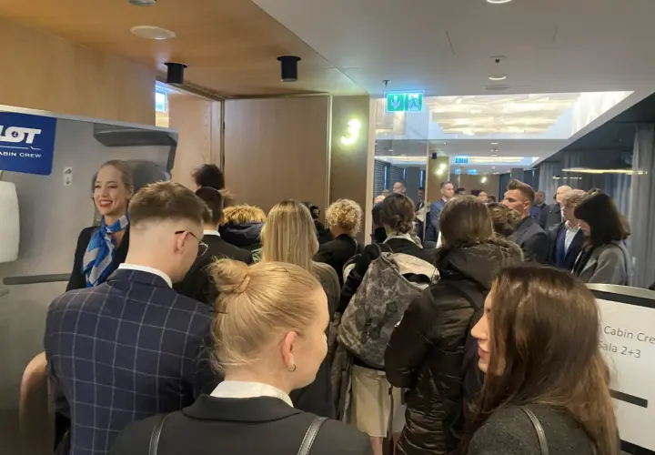 Uśmiechnięta stewardessa LOT Cabin Crew wita grupę osób. Marzenie o pracy w przestworzach zaczyna się tutaj.