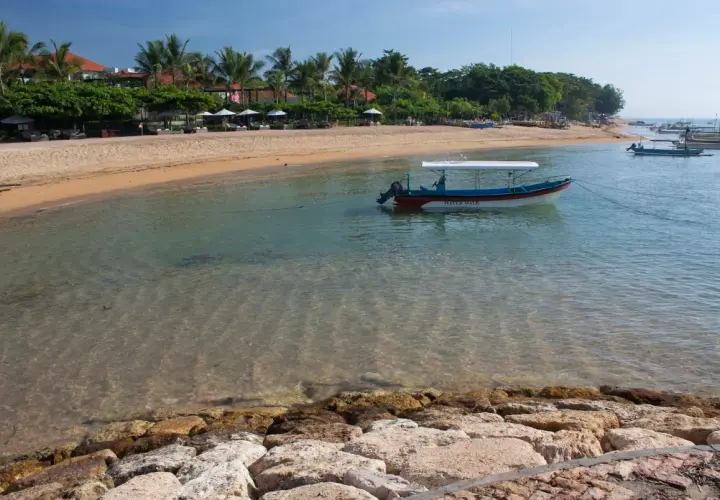 Spokojna zatoka w Sanur z łodzią "Water Walk" kołyszącą się na turkusowej wodzie. Piękna plaża z palmami i leżakami w tle.