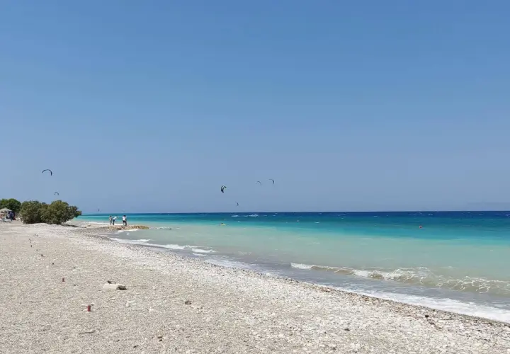 Plaża w zatoce Ialyssos, z turkusową wodą i kilkoma kitesurferami na horyzoncie.