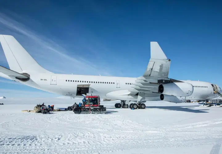 Biały airbus a340-300 na śniegu, z obsługą naziemną i ratrakiem.
