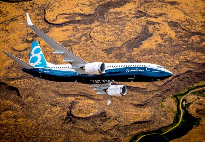 Boeing 737 MAX 8-200 z niebieskim ogonem z cyfrą 8 leci nad pustynnym krajobrazem.