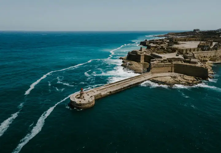 Malta: malta ile się leci? Widok na fortyfikacje i latarnię morską nad turkusowym morzem.